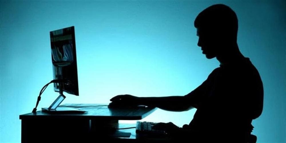 Ragazzo in controluce seduto davanti al computer in una stanza buia