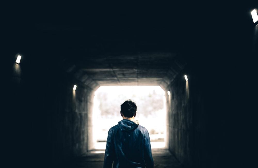 Ragazzo di spalle in un sottopasso buio, rivolto verso l'uscita illuminata
