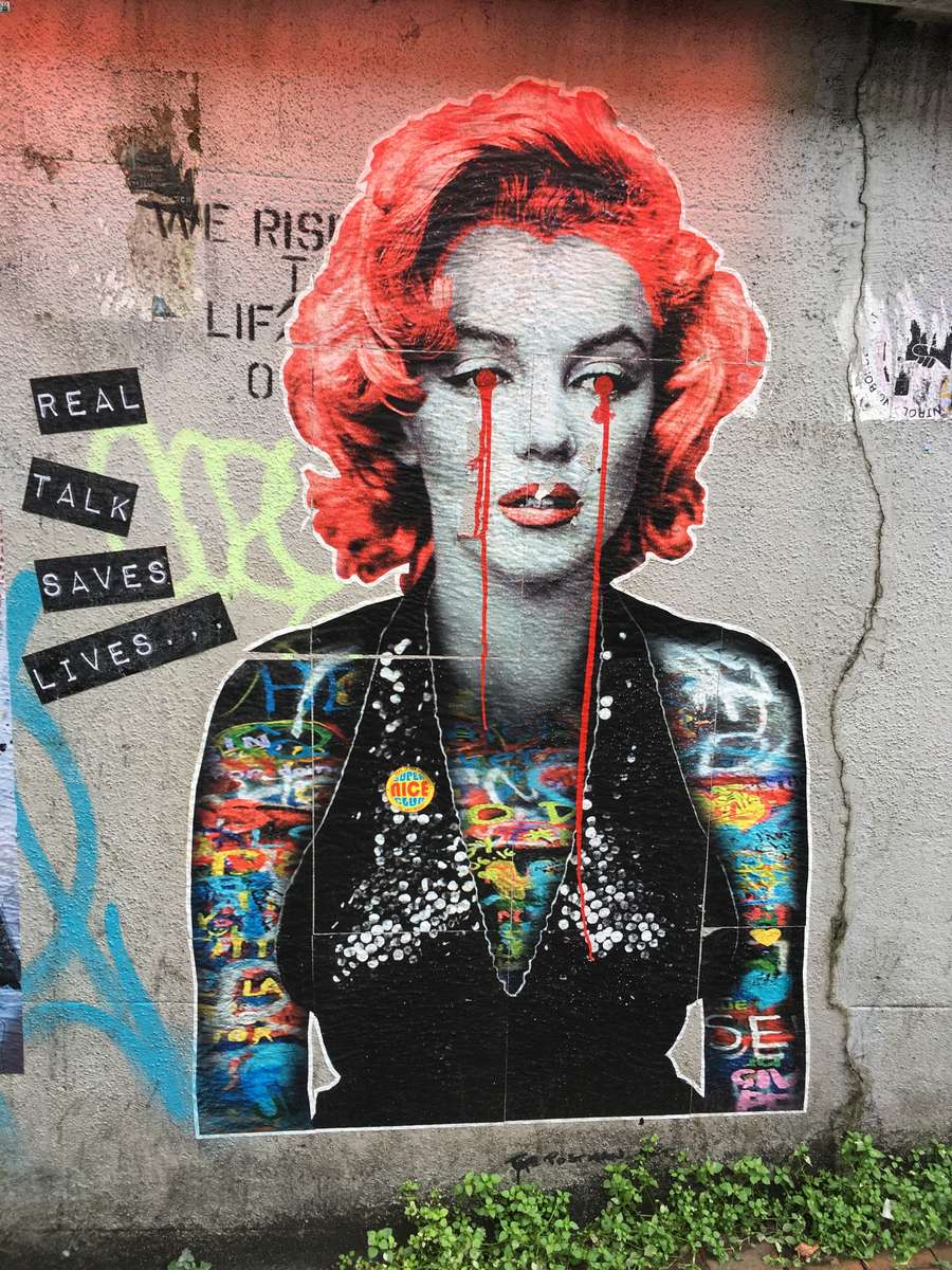 Murale con il ritratto di Marilyn Monroe che piange lacrime rosse, accanto alla scritta 'Real talk saves lives'